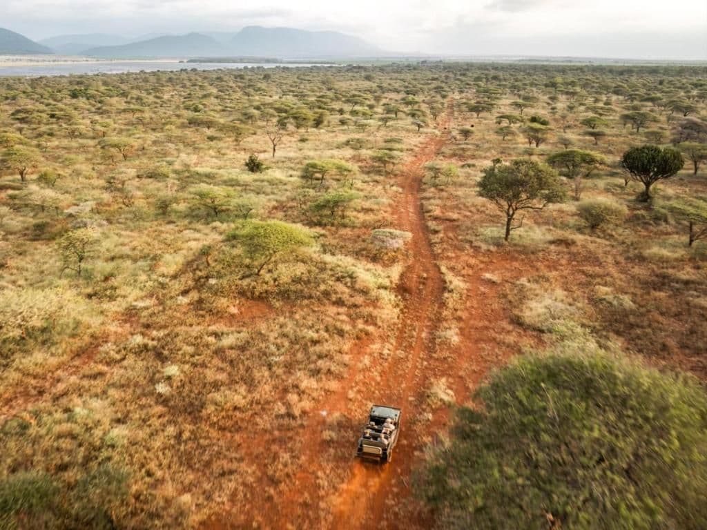 Aerial view of a red dirt road cutting through open savanna bushland near Nsoko, Eswatini, with a safari vehicle driving along it and distant hills on the horiz
