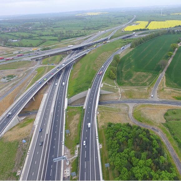 Aerial view of a multi-lane highway interchange with overpasses cutting through flat, green agricultural countryside under an overcast sky.