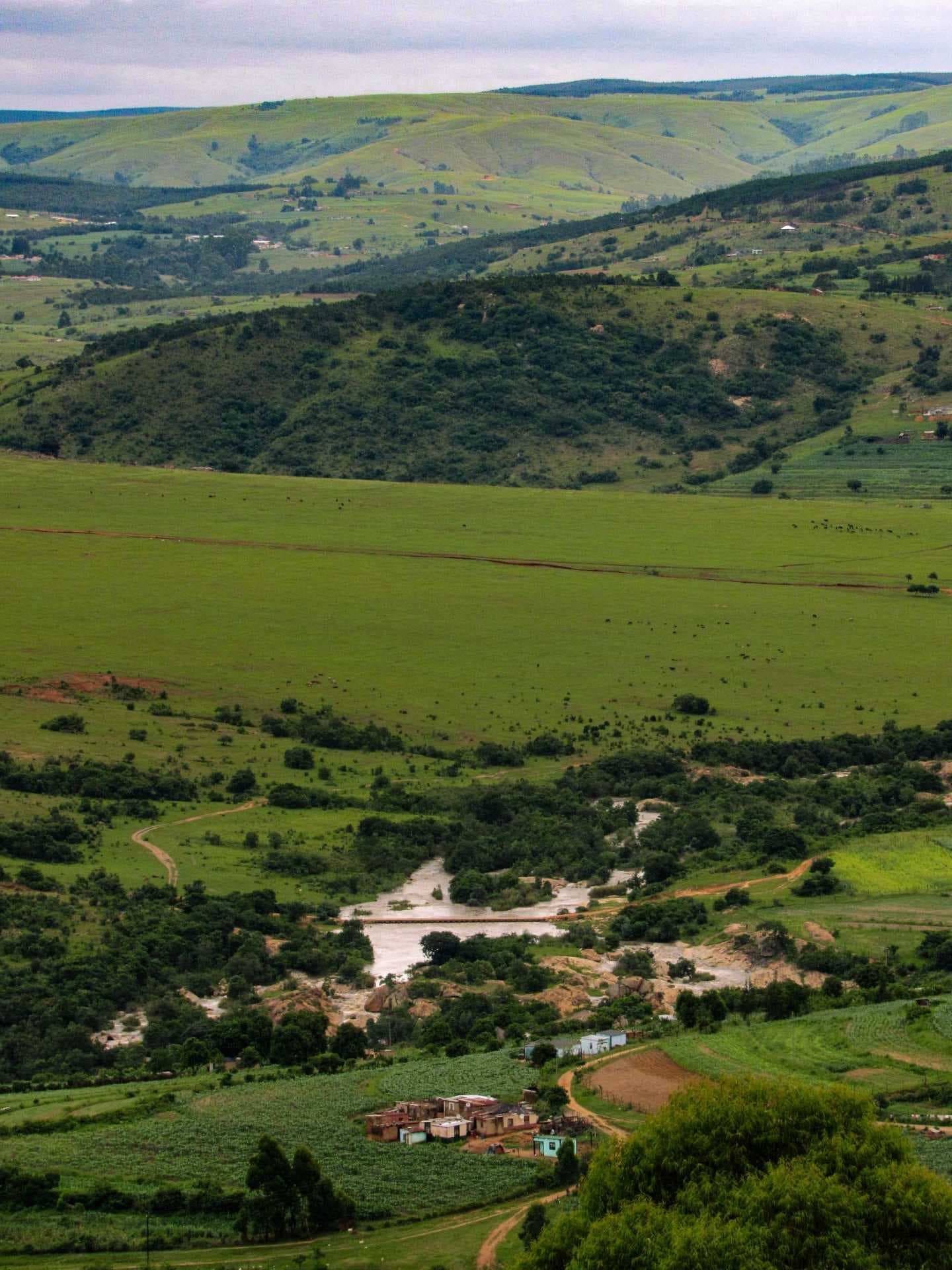 Wide landscape of green highland hills, valleys, a river, and scattered rural buildings in Eswatini