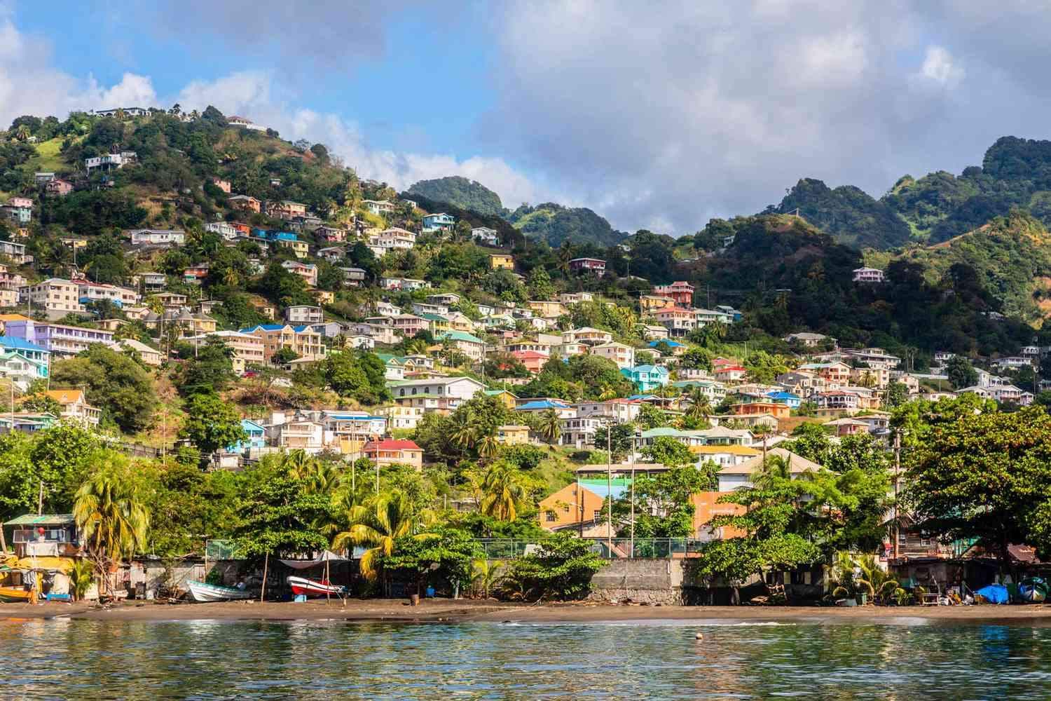 Coastal hillside town of Barrouallie, Saint Vincent and the Grenadines, with colorful houses, lush vegetation, boats on shore, and water in the foreground.