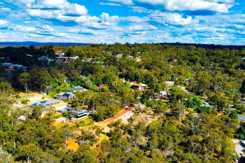 Aerial view of the green, tree-covered Gooseberry Hill ridge with scattered houses and dirt roads under a partly cloudy blue sky.