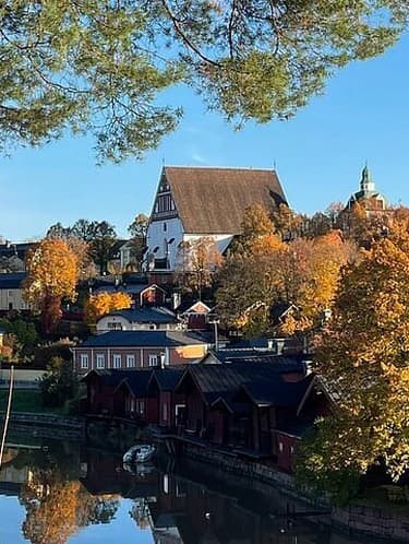 Wide autumn view of Multia's lakeside town center, featuring a white church, red waterfront buildings, and colorful trees reflected in the water.