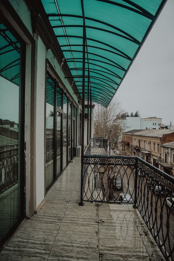 Elevated view from a balcony with a green canopy overlooking a street with parked cars and historic buildings in Baghdati town.