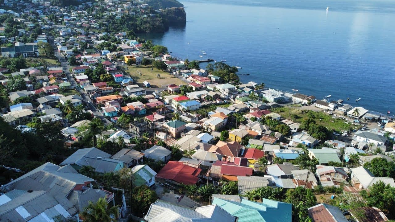 Aerial view of Barrouallie, Saint Vincent and the Grenadines, showing colorful houses, streets, and waterfront buildings along a calm bay.