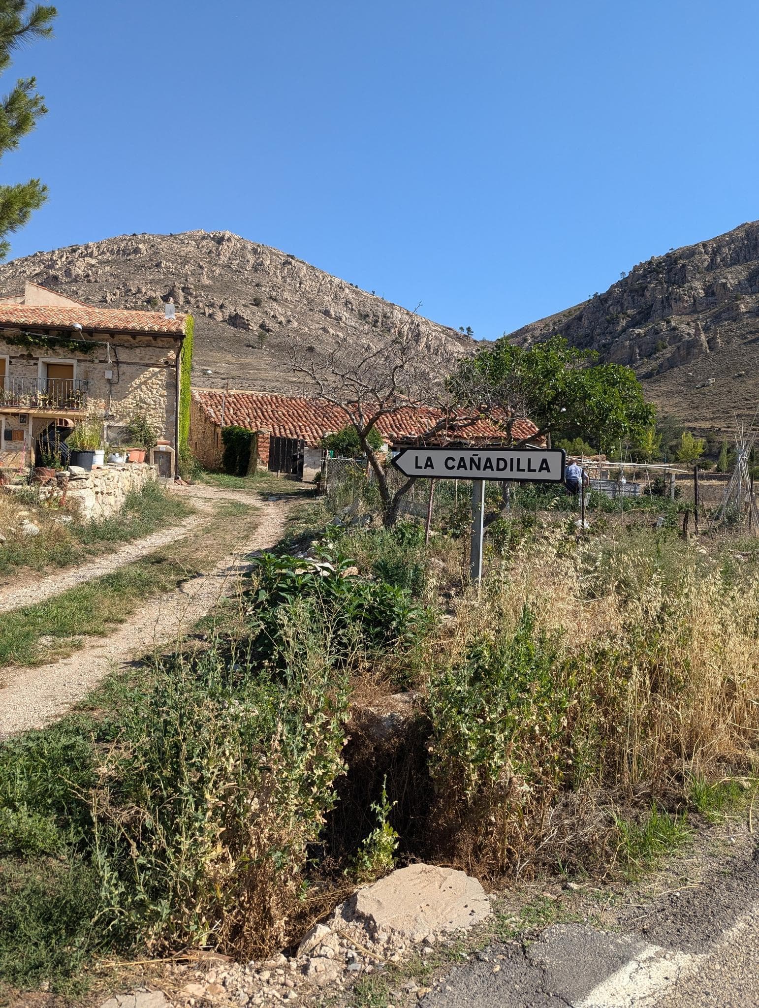 Rural stone dwelling with terracotta roof and 'La Cañadilla' sign, set against arid mountains under a clear blue sky.