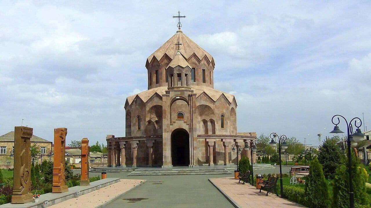Stone Armenian church with a cross-topped dome and surrounding plaza, benches, and carved pillars in Aghavnatun, Armenia.