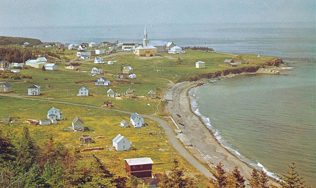 Aerial view of a small coastal village with white houses and a church on green hills beside a calm bay