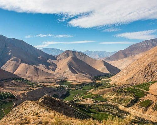 Aerial view of the Valle del Huasco, Provincia de Copiapó, Chile, with green cultivated fields and orchards nestled between arid mountains under a blue sky.