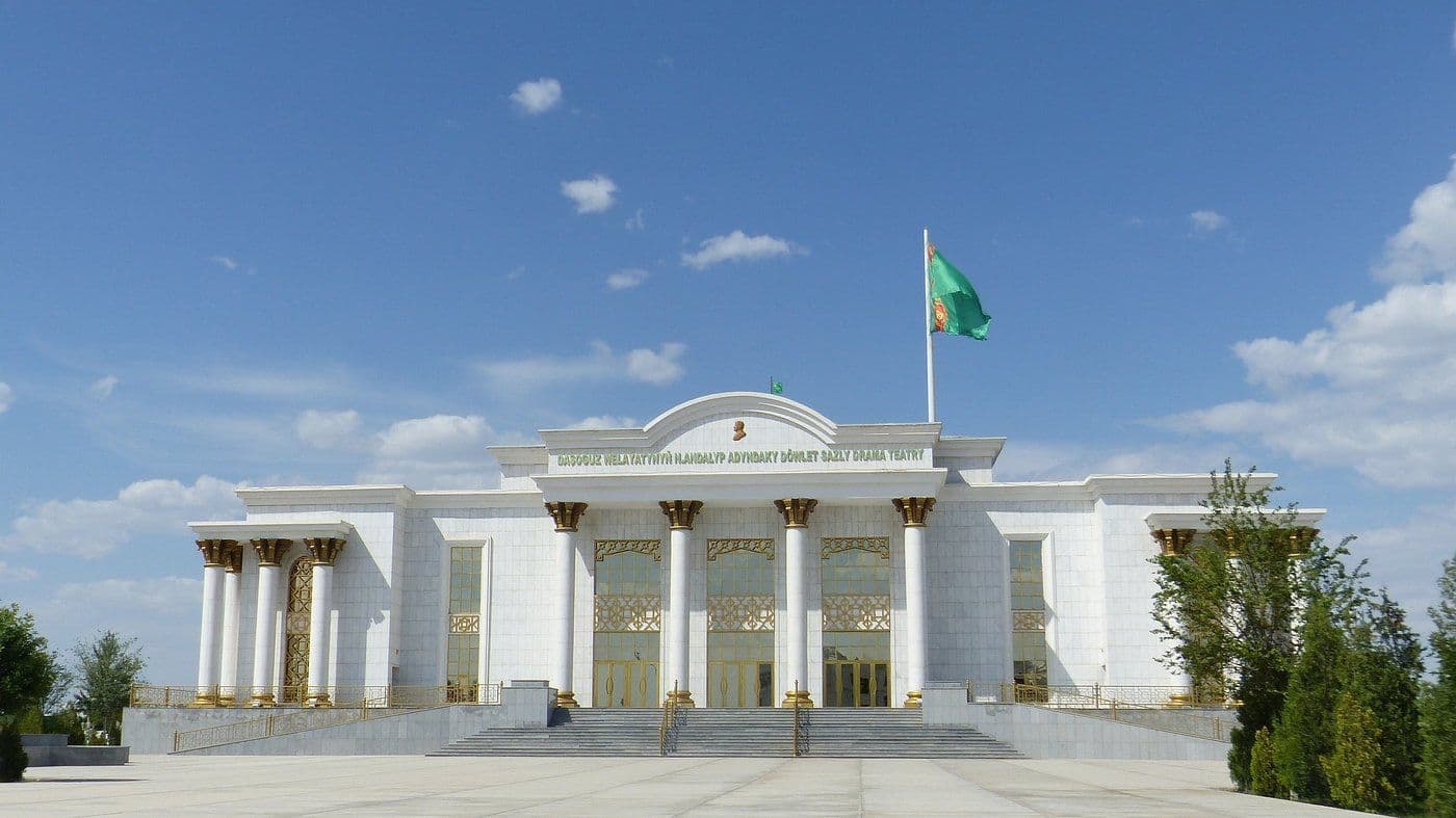 White neoclassical administrative building with columns, gold accents, and a flag under a blue sky.