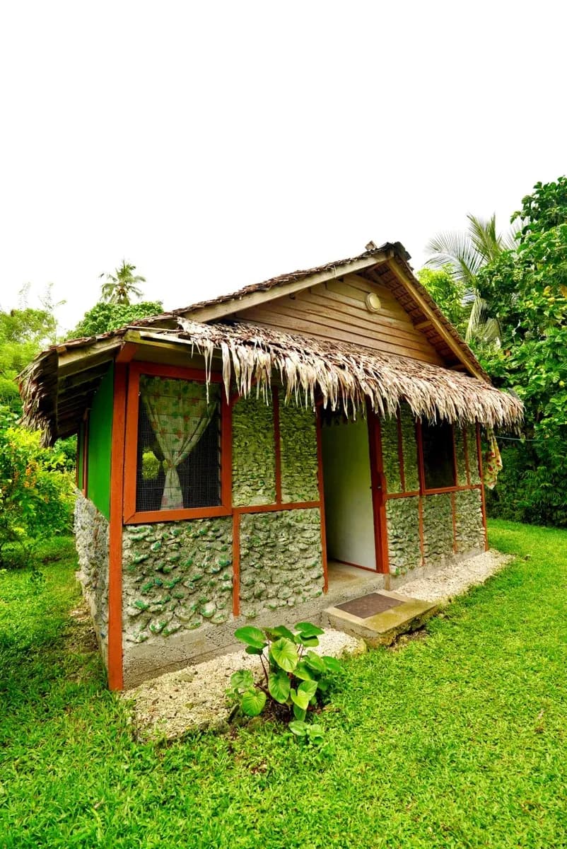 Small rustic guesthouse with thatched roof and shell-stone walls in a tropical garden setting in Vanuatu