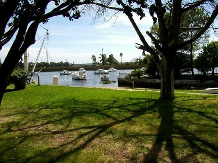 Calm Santa Lucía River near Santiago Vázquez with moored boats on a grassy bank framed by tree shadows