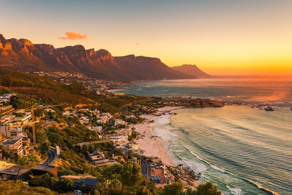 Aerial coastal view of Mossel Bay at sunset, showing shoreline, town edge, and surrounding mountains.