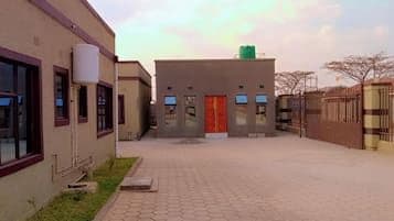 Exterior view of a paved courtyard with low-rise buildings, a red door, and a gate under a bright sky in Chililabombwe, Zambia.