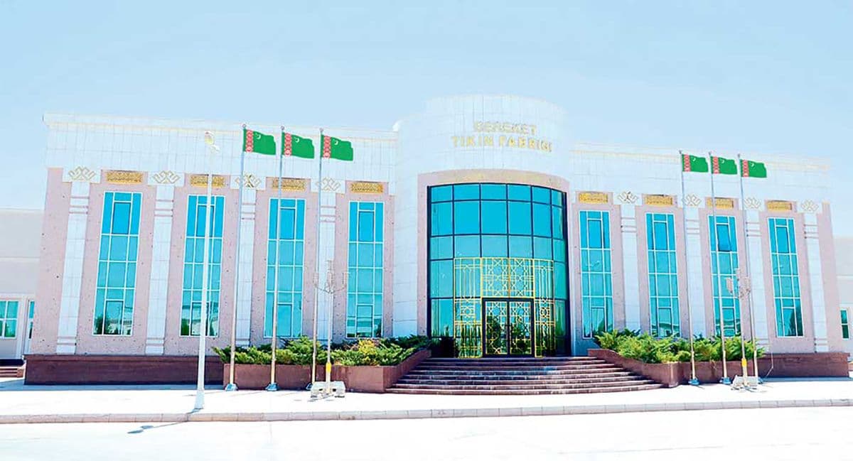 Modern government building facade in Bereket with Turkmen flags, glass entrance, and clear sky.
