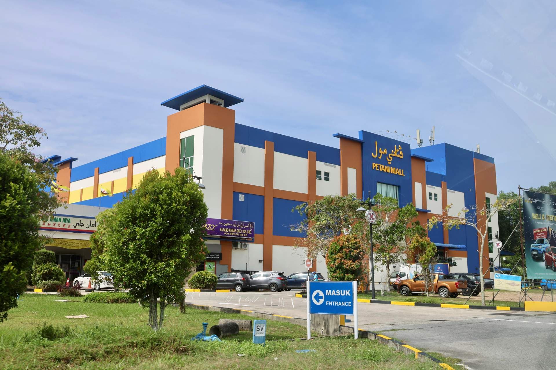 Exterior view of Petani Mall with blue and orange facade, entrance sign, and parked cars under a clear sky.