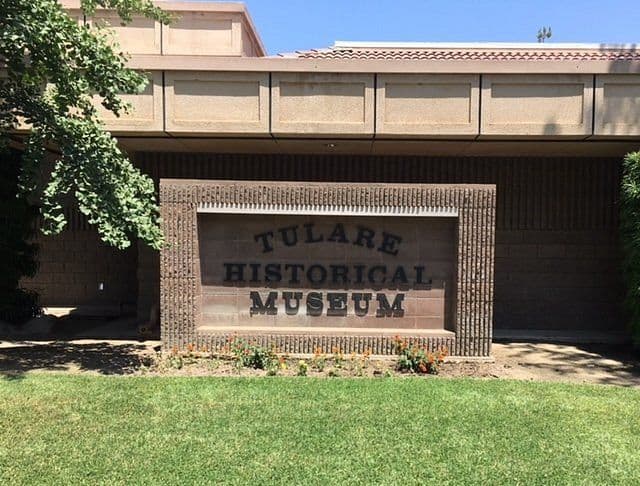Exterior view of the Tulare Historical Museum sign on a brick wall, with lawn and building facade.