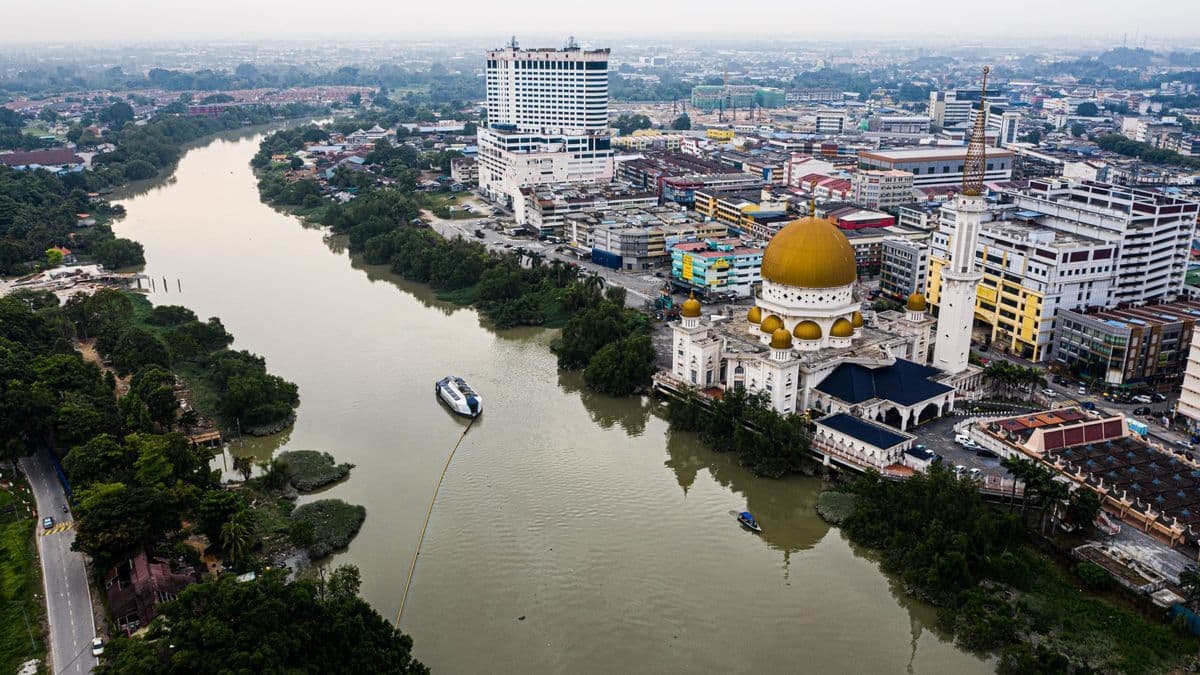 Aerial daytime view of the Klang River with a boat, town skyline, and a prominent gold-domed mosque.