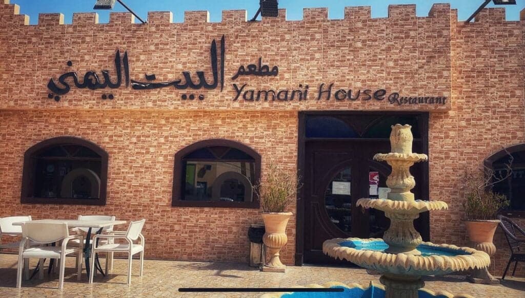 Exterior of Yamani House Restaurant featuring a brick facade, Arabic signage, and a tiered stone fountain in the courtyard.