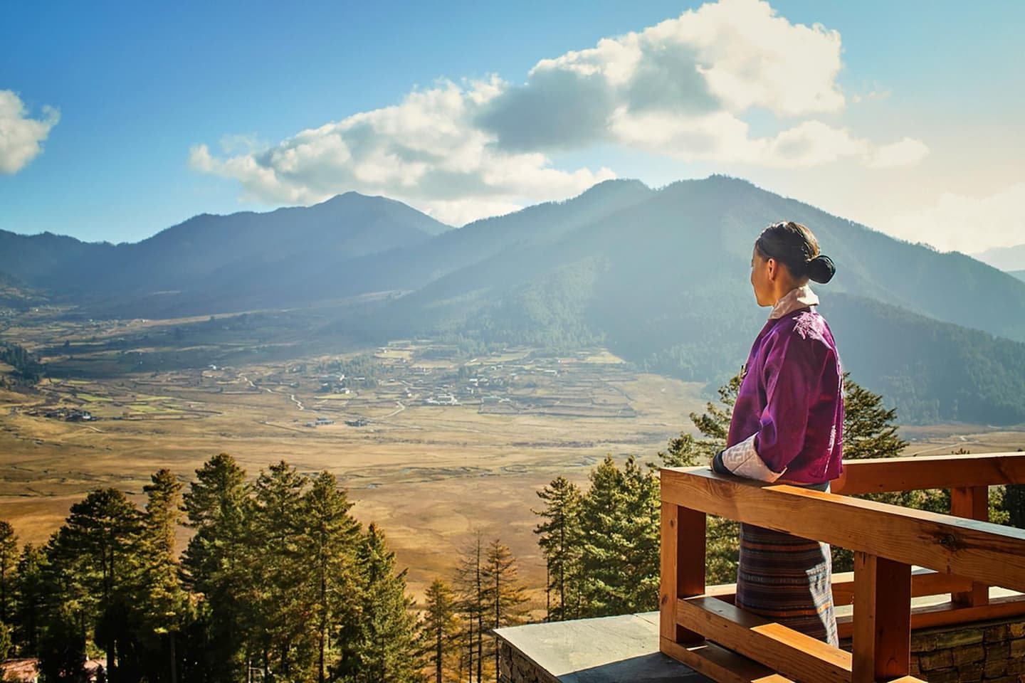 Wide autumn valley view from a wooden railing in the Tsirang district, Bhutan, with rolling hills and distant mountains.