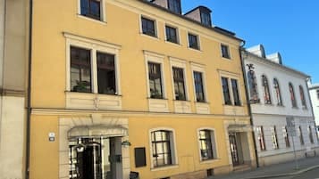 Street view of a yellow building with white trim and a white building on a sunny day.