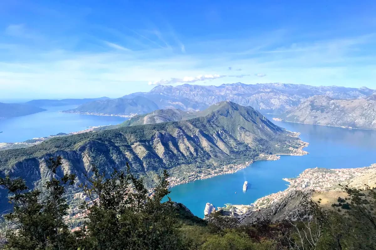 Aerial coastal view of the Bay of Kotor with Tivat, green mountains, blue water, and clear sky.
