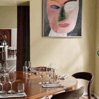 A dining table set with glassware and cutlery in a restaurant, featuring a large abstract portrait painting on the wall.