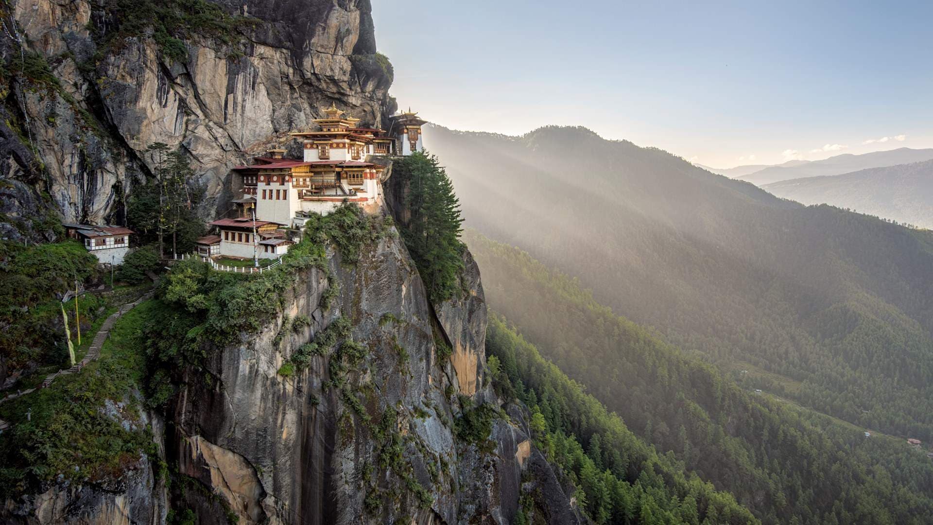 Wide photograph of Tiger's Nest Monastery perched on a cliff above a misty forested valley.