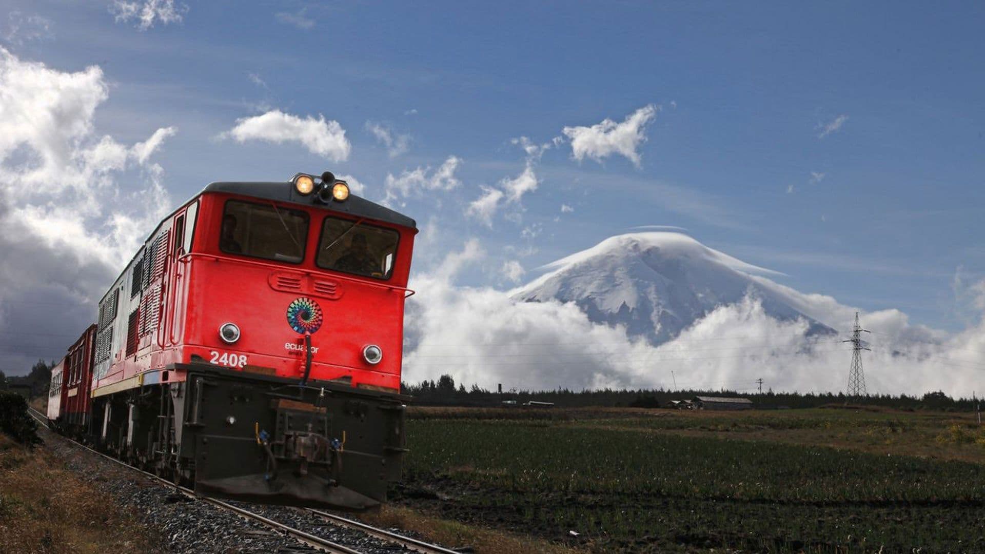 Red Ecuadorian locomotive travels on tracks through green fields, with a snow-capped volcano and clouds in the background along the Trans-Andean Railway serving