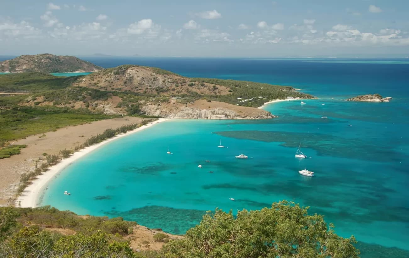 Aerial view of a tropical bay with turquoise water, white sand beach, boats, and green hills near Kirakira, Makira.