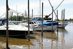 Sailboats moored in a small muddy river harbor at Santiago Vázquez with wooden pilings and distant green shoreline