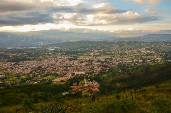 Aerial view of a small town nestled in a green valley with rolling hills and dramatic clouds.