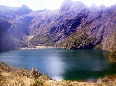 A scenic wide landscape view of a deep blue alpine lake surrounded by steep, rugged mountain slopes and highland vegetation.